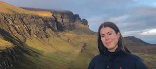 A fermale student standing in front of green Scottish mountains 