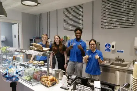 Four people standing in front of a food counter smiling with a thumbs up. 